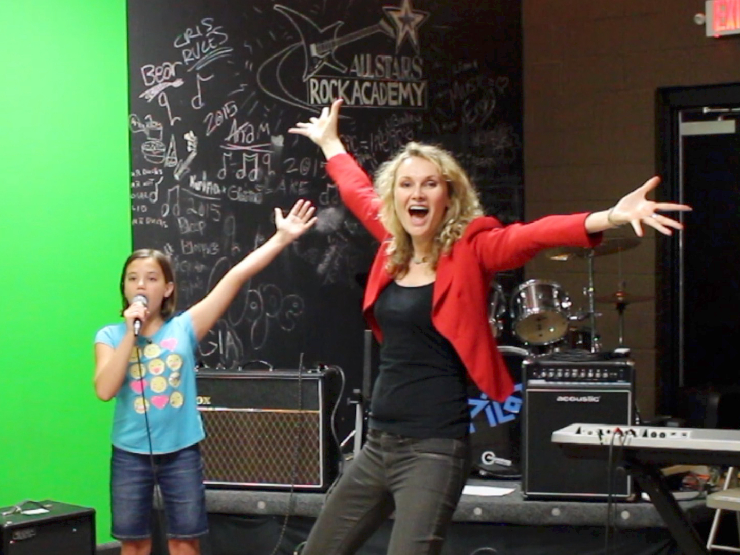 Juliana Polansky coaching a young singer with open-armed stage presence at a rock academy