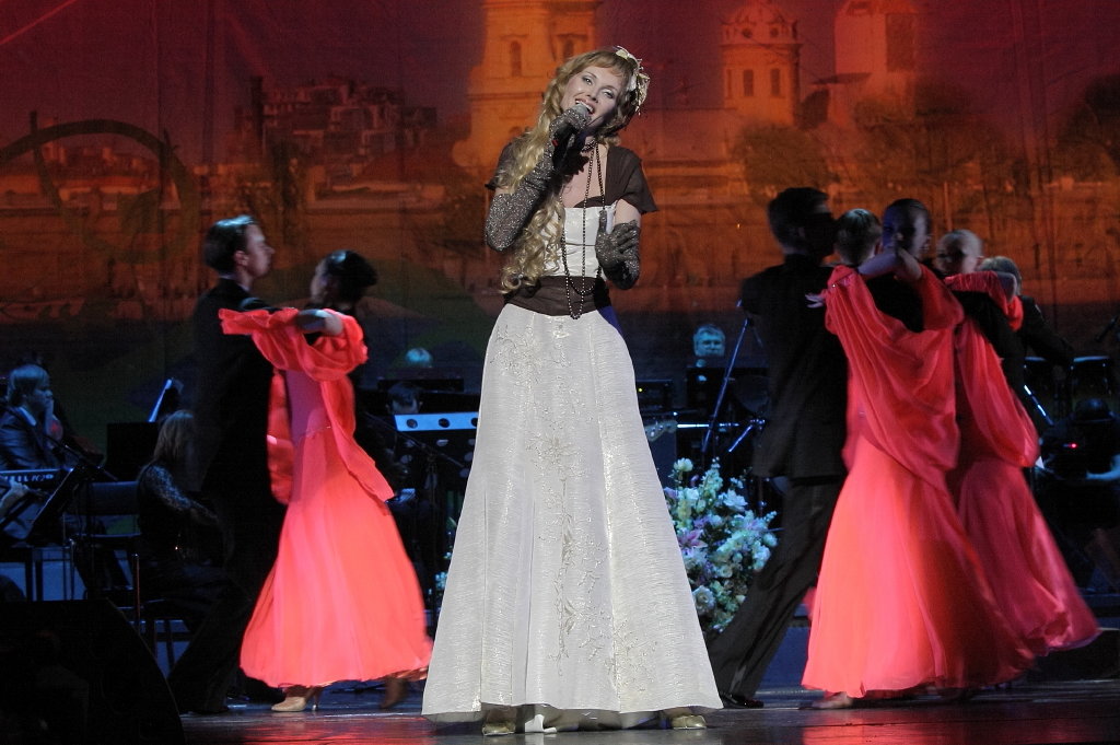 Juliana Polansky in a white gown performing a concert number with dancers on stage